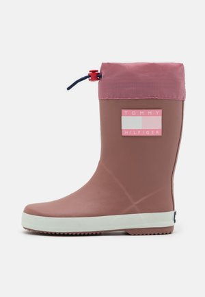 Mellem høj lavendelfarvet gummistøvle med hvid sål, lyserød stofmanchet, justerbar snøre og Tommy Hilfiger logo-patch på siden.