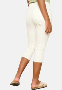 Pantalones capri blancos confeccionados en tela elástica, con una cintura de altura media, bolsillos traseros y aberturas en los dobladillos, combinados con sandalias tipo slide.