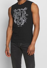 Camiseta de algodón sin mangas de color negro con un diseño gráfico gris que presenta serpientes y la palabra "REPLAY" en forma de diamante.