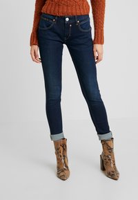 Smala jeans i mörk denim med sömnadsdetaljer, femficksdesign och en upprullad kant. I kombination med bruna ankelboots med ormskinnsmönster.