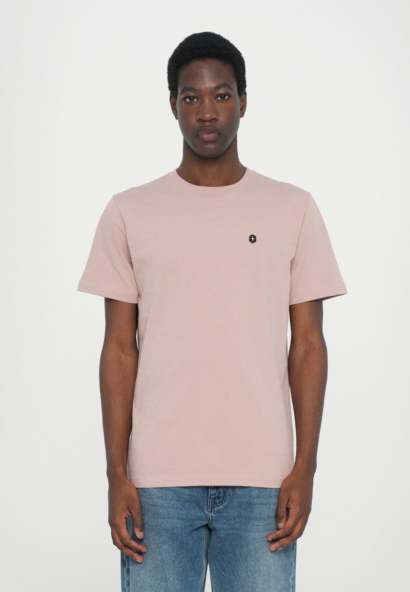 Helles pinkes T-Shirt mit kurzen Ärmeln aus Baumwolle, mit rundem Ausschnitt und kleinem schwarzen Logo auf der linken Brustseite.