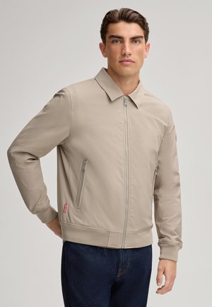 Beige ritsjack met kraag, zijritszakken, ribgebreide manchetten en zoom; gladde textuur met minimalistische ontwerpaccenten.