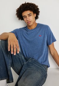 Sinine puuvillane T-särk ümmarguse kaelusega ja lühikeste varrukatega, millel on väike punane Levi'si logo silt. Kandmise koos lahtiste teksapükstega.