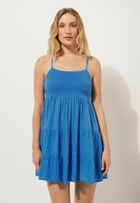Vestido azul de tirantes finos con volantes, que presenta un cuerpo fruncido y una tela ligera. La textura parece suave y transpirable.