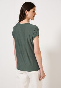 T-shirt vert forêt à manches courtes, présentant une coupe décontractée et un col rond, fabriqué en tissu doux et léger, avec des poignets de manches roulés.