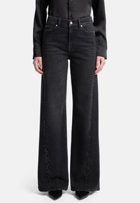 Czarne szerokie jeansy o wysokim stanie z misternymi wycięciami po bokach i denowym materiałem. Do tego czarne, spiczaste buty.