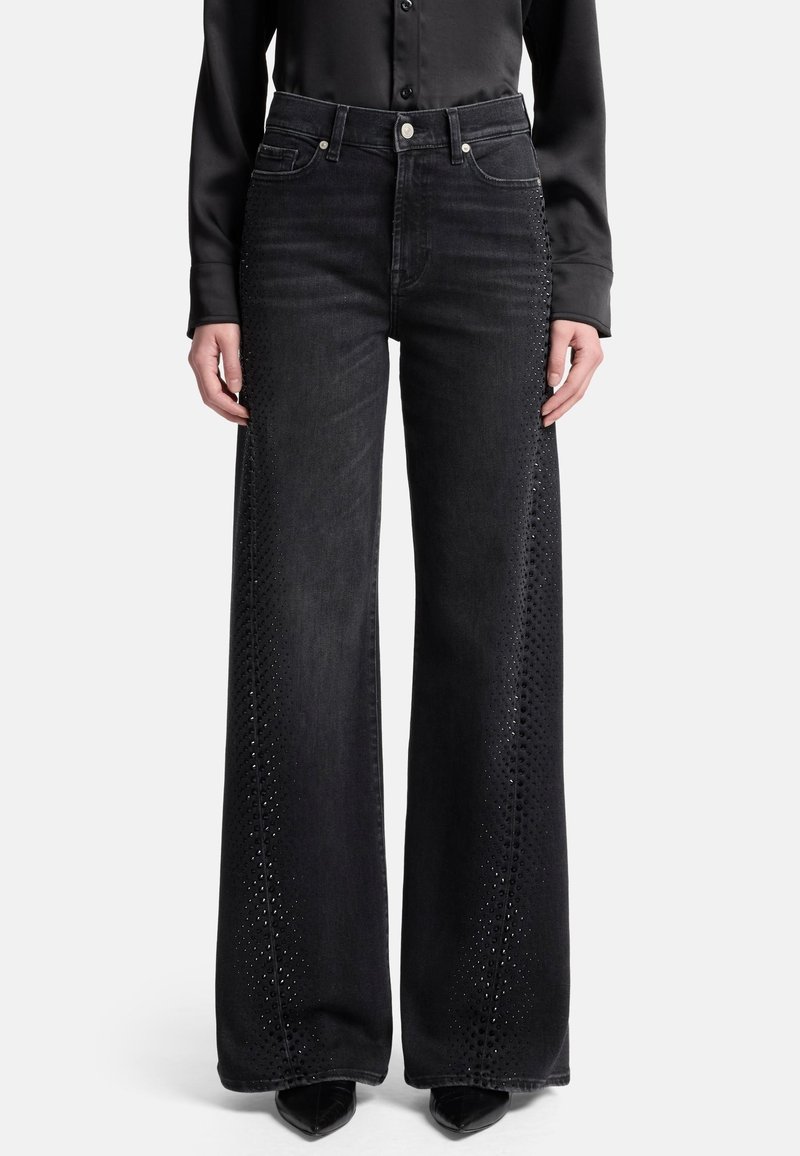 Czarne szerokie jeansy o wysokim stanie z misternymi wycięciami po bokach i denowym materiałem. Do tego czarne, spiczaste buty.