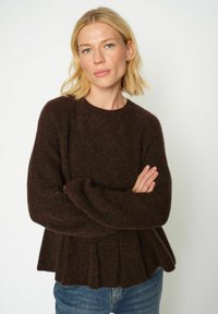 Hnědý pletený svetr s kulatým výstřihem, dlouhými rukávy a peplum lemem; texturovaný, měkký vzhled; kombinováno s modrými džíny.