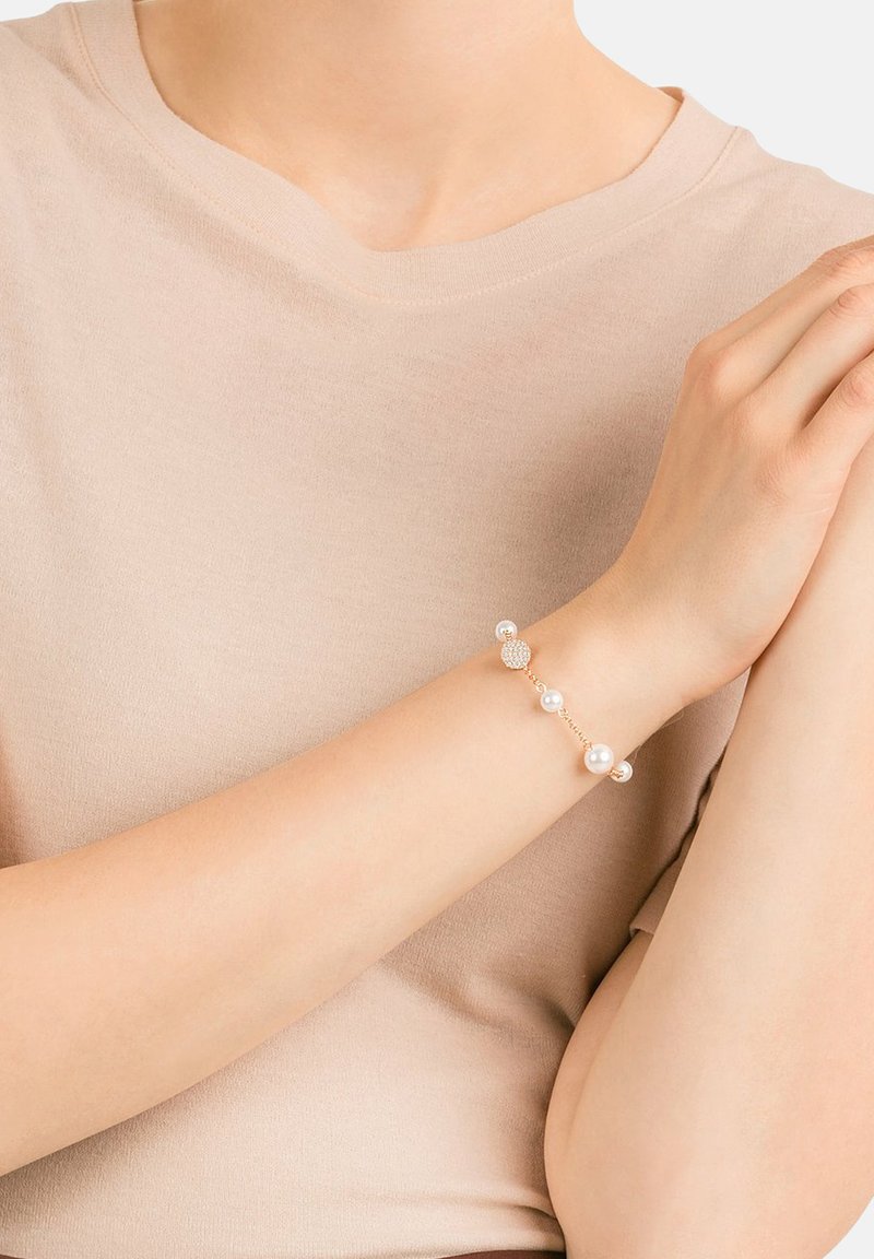 Bracelet en or délicat avec cinq perles blanches rondes et un accent en cristal rond, porté sur un haut beige discret.