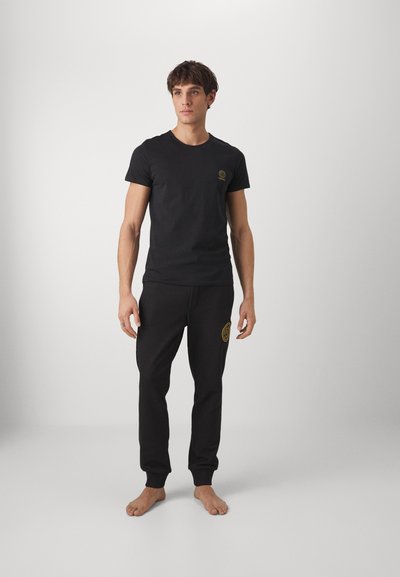 T-shirt en coton noir associé à un pantalon de jogging noir, avec un petit logo doré sur la poitrine et un plus grand logo doré sur la jambe gauche.