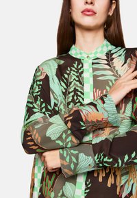 Button-up shirt with a dark brown background, featuring green botanical patterns, contrasting checkered collar, and cuff accents.