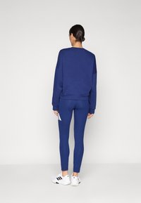 Sweatshirt azul-marinho com corte solto, combinado com leggings azul-marinho ajustadas com detalhes brancos e sapatilhas brancas de desporto.