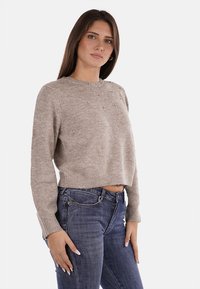 Maglione corto color marrone chiaro con sottili dettagli di perline sul petto. Realizzato in un tessuto morbido, presenta un classico collo rotondo e polsini a coste.