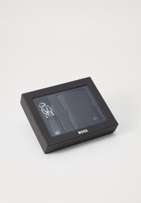 Cutie neagră pentru cadouri care conține un portofel negru elegant și un breloc argintiu. Portofelul are un model texturat și un detaliu cu logo pe partea din față.