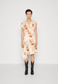 Rochie cu mânecă scurtă în crem cu modele abstracte portocalii, având decolteu în V și margine asimetrică, asortată cu cizme negre de cowboy.
