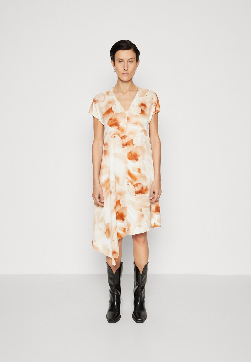 Rochie cu mânecă scurtă în crem cu modele abstracte portocalii, având decolteu în V și margine asimetrică, asortată cu cizme negre de cowboy.