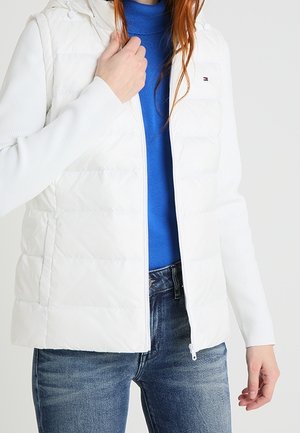 White puffer vest with a zip front, made of quilted material. Features a hood and ribbed sleeves, layered over a blue top.