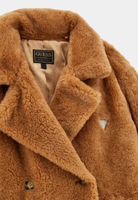 Cappotto in pelliccia sintetica marrone con design doppiopetto, colletto a revers e accento con logo argentato. Foderato con un tessuto beige liscio.