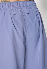 Shorts violets clairs avec une taille élastique, fabriqués dans un tissu léger et lisse qui a un léger éclat. Comprend un détail de poche arrière.