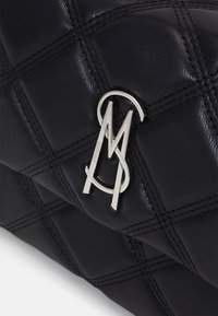 Sac à main en cuir matelassé noir avec un logo en métal argenté distinctif et un design structuré souligné par des coutures accentuées.