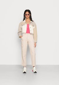 Casaco cropped em vários tons, em bege e branco, top justo rosa, calças cargo bege claro e ténis chunky com detalhes em rosa e amarelo.