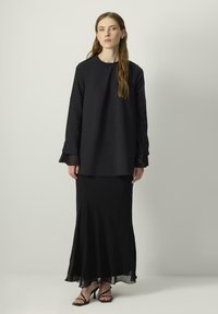 Black long-sleeve top with a loose fit, paired with a flowing black skirt featuring a sheer hem. The outfit is completed with black strappy heels.