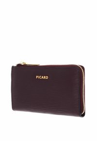 Portefeuille en cuir bordeaux avec une texture côtelée, fermeture éclair dorée et logo embossé sur le devant. Forme rectangulaire compacte.