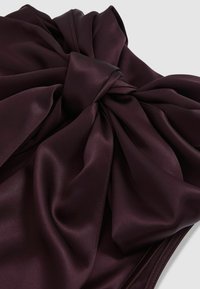 Satin audums dziļi burgundijas krāsā ar lielu mezgla detaļu centrā, izceļot gludu tekstūru un elegantu kritumu.