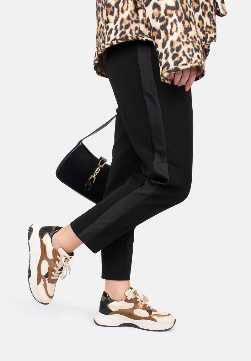 Pantaloni neri a sigaretta con strisce laterali in satin, abbinati a sneakers beige e marroni con un design a trama mista e lacci. Borsa nera.