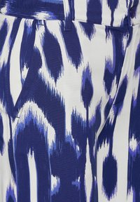 Niebiesko-biała tkanina wzorzysta o teksturowanym designie, z wyraźnymi, abstrakcyjnymi kształtami oraz detalami takimi jak kieszenie i szwy.