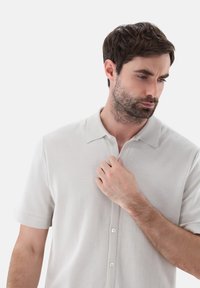 Polo shirt grigio chiaro a maniche corte realizzato in tessuto morbido, con apertura a bottoni, colletto classico e texture sottile.