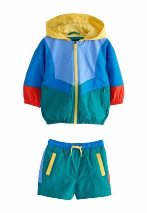 Ensemble deux pièces pour enfants comprenant une veste coupe-vent multicolore avec capuche jaune et fermeture éclair, accompagnée d'un short bleu sarcelle avec cordon de serrage jaune et poches.