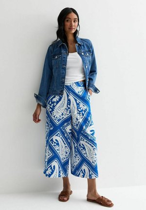 Denim jacket, white tank top, and blue patterned culotte pants with floral motifs. Brown sandals complete the outfit. Flat texture, casual style.