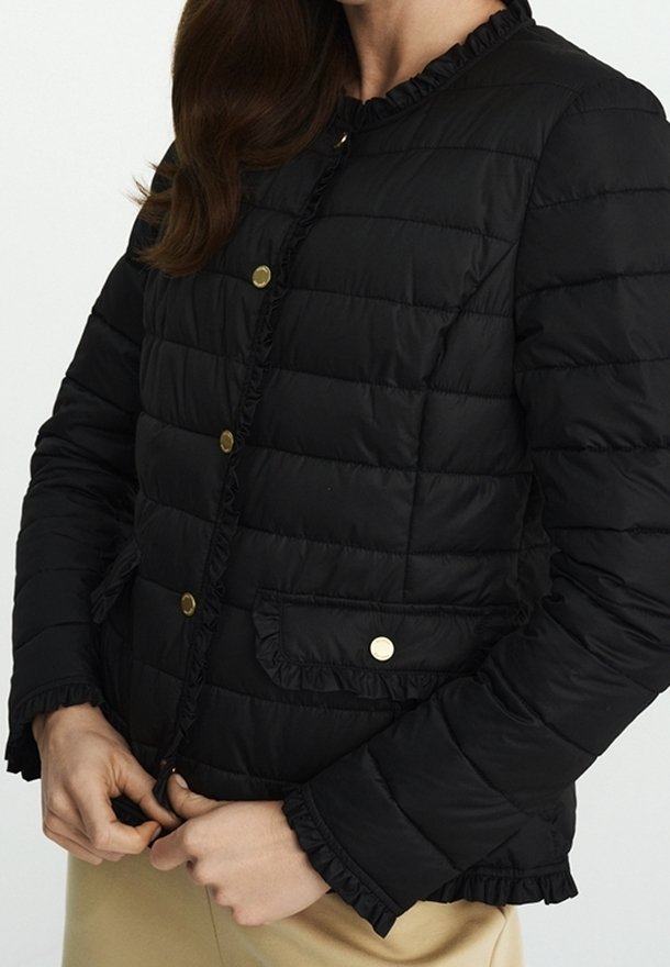 Černá prošívaná bunda s volány na okrajích, zlatými patentkami a předními kapsami. Tkanina má hladký povrch s lehkým vzhledem.