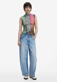 Multicolored tank top with abstract patterns, paired with light blue wide-leg jeans. The fabric appears soft and slightly sheer.