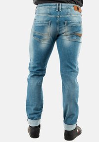 Jeans en denim bleu clair avec une finition délavée, dotés d'une coupe droite, de bas de pantalon retroussés, et d'un patch en cuir marron au-dessus de la poche arrière droite.