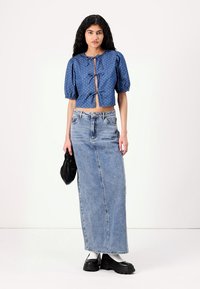 Blå prickig puffärm croptop med knytning fram, i kombination med en högmidjad denimmaxikjol. Tillbehören består av en svart väska och kraftiga skor.