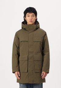 Parka olive vert avec un col haut, des poches à rabat �à l'avant, une capuche avec cordon de serrage réglable et une silhouette moderne et épurée.