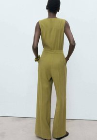 Olive green jumpsuit with wide legs, sleeveless design, and a fitted waist, made of smooth fabric with a clean back.