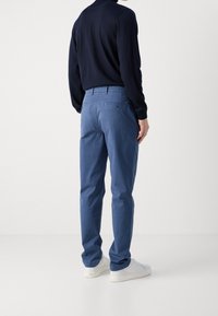 Pantaloni chino in cotone blu con taglio slim, design a cinque tasche e dettagli discreti sulle tasche posteriori, abbinati a sneakers bianche e una maglia navy.