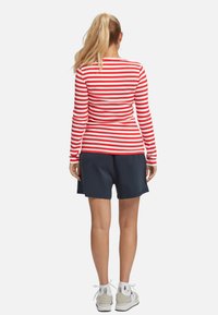 Roter und weiß gestreifter Langarm-Shirt mit taillierter Passform, kombiniert mit navy-blauen Shorts. Die Schuhe haben eine weiße Basis mit grauen Akzenten.