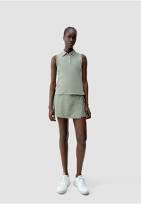 Lichtgroene polo met kraag, met drie knopen en een gelaagd uiterlijk boven een bijpassende rok. Witte sneakers maken de outfit compleet.