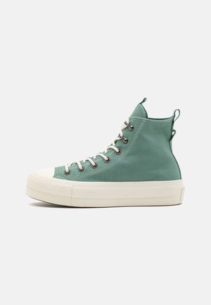 Zapatillas altas de lona en color verde azulado con suela de goma blanca. Presenta ojales de metal, cordones blancos y lazos en el collar para facilidad de uso.