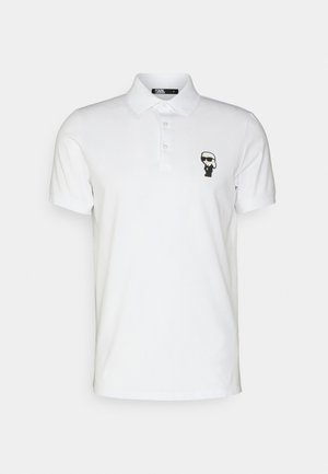 Polo shirt blanc en coton, avec un graphisme noir d'une silhouette portant des lunettes de soleil sur la poitrine gauche. Col classique avec trois boutons.