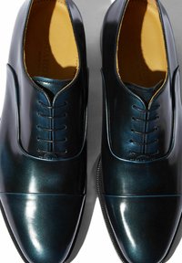 Oxfords en charol azul oscuro, con un acabado suave, punta redondeada, seis ojales y un sutil detalle de costura, con un interior en contraste en tono marrón claro.