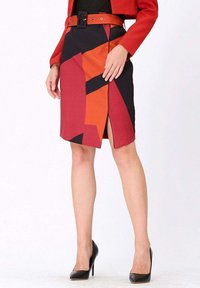 Jupe crayon à motif géométrique noir, rouge et orange avec une fente sur le côté, portée avec un haut noir et un blazer rouge, mettant en avant une ceinture large.