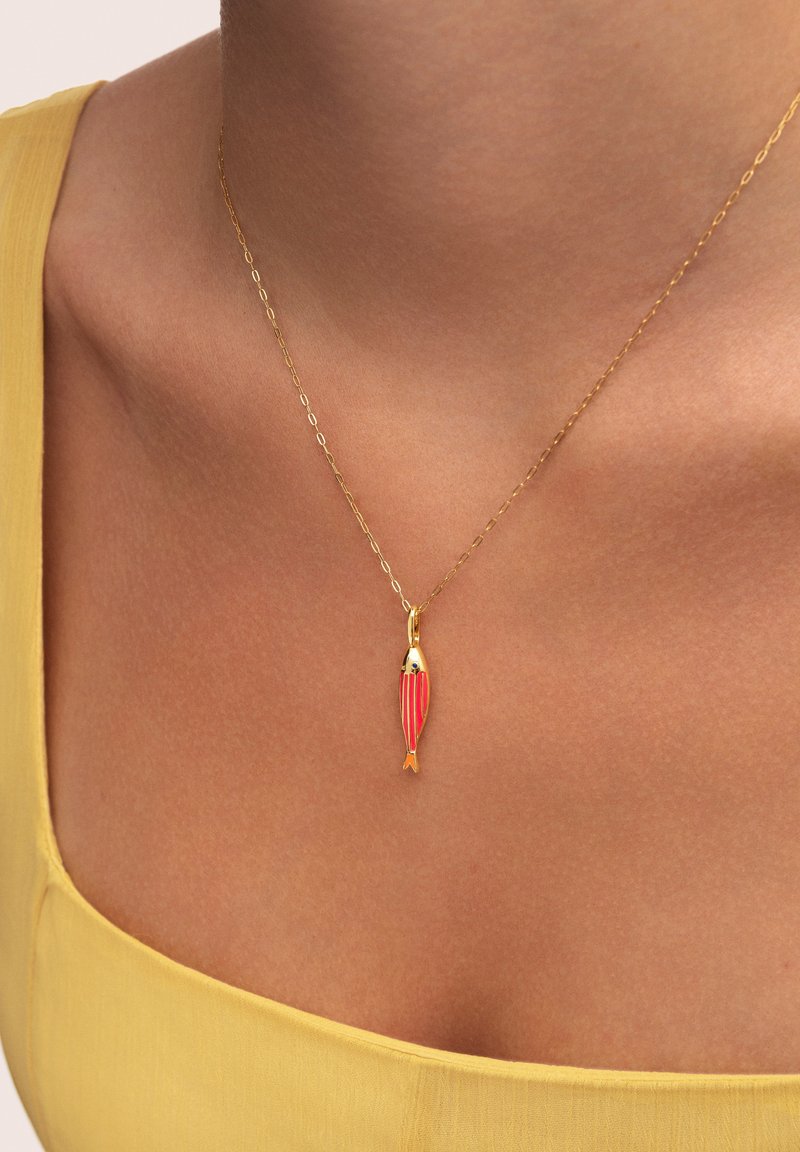 Collier en or avec un pendentif en forme de poisson, le tout orné de rayures rouges et de petits détails. L'arrière-plan est d'une teinte claire et unie.