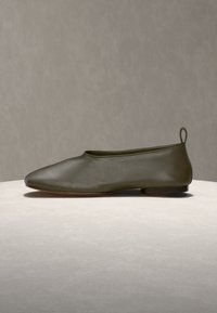 Chaussure plate en cuir vert olive foncé, bout arrondi et petit talon, exposée sur une surface claire contre un fond neutre.