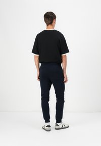 Schwarzes kurzärmliges T-Shirt mit weißem Besatz, kombiniert mit marineblauen Slim-Fit-Jogginghosen und weißen Sneakers mit schwarzen Akzenten.