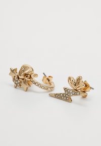 Gouden oorbellen met een sterontwerp met strass accenten en de vorm van een bliksemschicht, met glanzend metaal en ingewikkelde details.